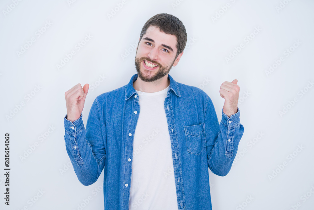 Young handsome hispanic man wearing denim jacket over white isolated background celebrating surprised and amazed for success with arms raised and open eyes. Winner concept. Young handsome hispanic man wearing denim jacket over white isolated background celebrating surprised and amazed for success with arms raised and open eyes. Winner concept.