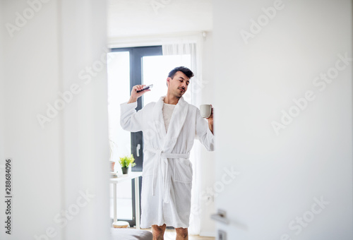 Young man with coffee and smartphone in the bedroom in the morning.