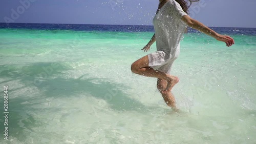 A beautiful young woman in white dress runs along waves of Turquoise ocean waters in the Maldives. Exotic tropical plants. Slow motion. Dream life. Happy summer vacation.