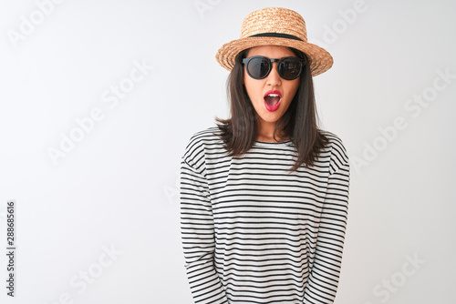 Chinese woman wearing striped t-shirt hat sunglasses standing over isolated white background afraid and shocked with surprise expression  fear and excited face.