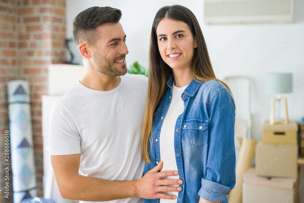 Fototapeta premium Beautiful young couple moving to a new house, smiling happy arround cardboard boxes