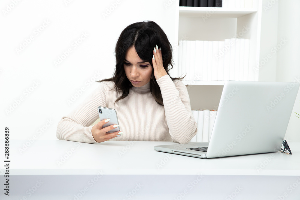 Unhappy and frustrated lady watching phone in office sitting infront of the computer Unhappy and frustrated lady watching phone in office sitting infront of the computer