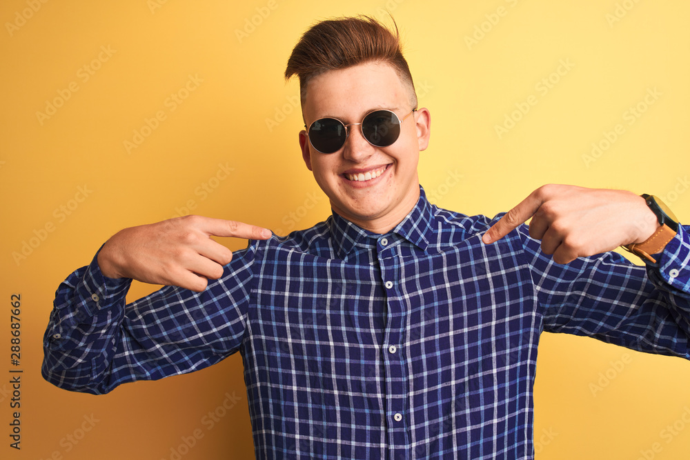 Young handsome man wearing casual shirt and sunglasses over isolated yellow background looking confident with smile on face, pointing oneself with fingers proud and happy. Young handsome man wearing casual shirt and sunglasses over isolated yellow background looking confident with smile on face, pointing oneself with fingers proud and happy.