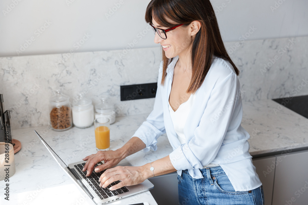 Smiling business woman indoors at home at the kitchen using laptop computer. Smiling business woman indoors at home at the kitchen using laptop computer.