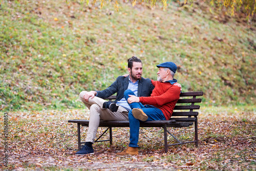 Senior father and his son sitting on bench in nature, talking.