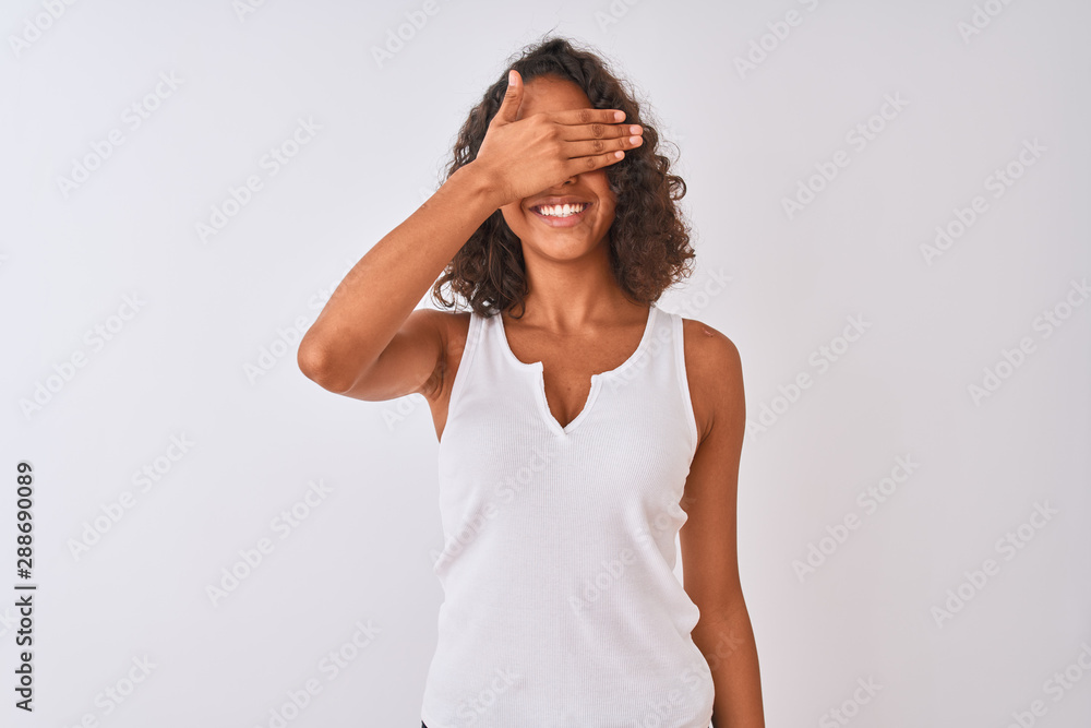 Young brazilian woman wearing casual t-shirt standing over isolated white background smiling and laughing with hand on face covering eyes for surprise. Blind concept. Young brazilian woman wearing casual t-shirt standing over isolated white background smiling and laughing with hand on face covering eyes for surprise. Blind concept.
