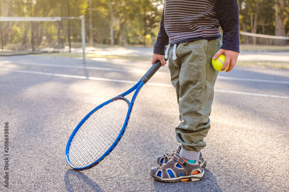 Little Australian boy with racket and ball at outdoor tennis court in Australia on a day
