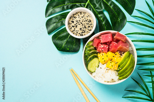 Tuna poke bowl with rice, avocado, mango and cucumber on blue. photo