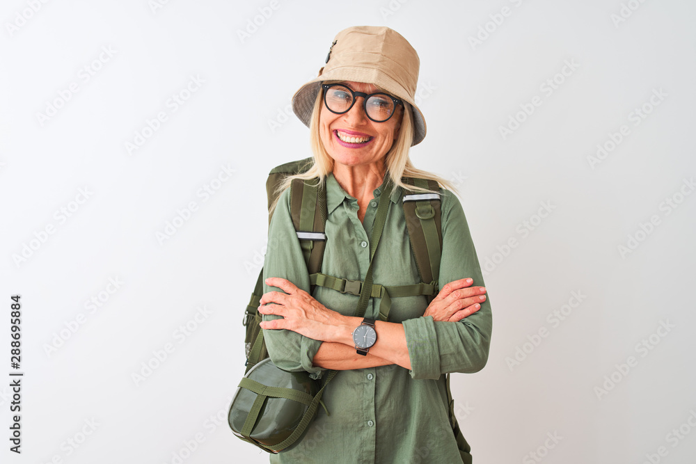 Middle age hiker woman wearing backpack hat canteen glasses over isolated white background happy face smiling with crossed arms looking at the camera. Positive person.