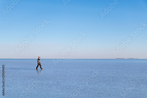 Young man walking and looking away with perfect blue sky reflection in Salar de Uyuni - Uyuni Salt Flats in Bolivia