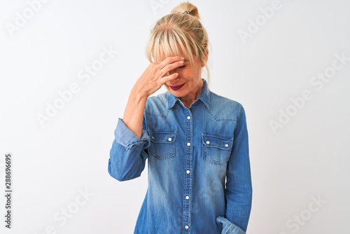 Middle age woman wearing casual denim shirt standing over isolated white background tired rubbing nose and eyes feeling fatigue and headache. Stress and frustration concept.