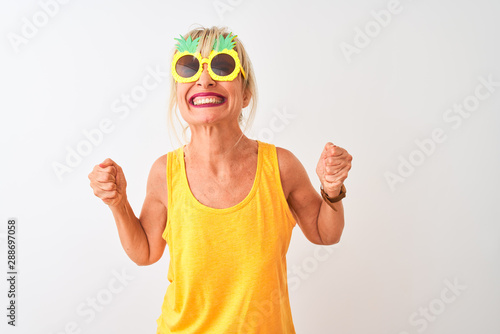 Middle age woman on vacation wearing pineapple sunglasses over isolated white background very happy and excited doing winner gesture with arms raised, smiling and screaming for success. 