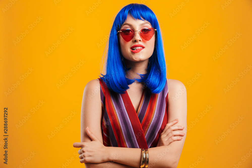 Portrait of cute seductive woman wearing blue wig and sunglasses looking at camera and biting her lip