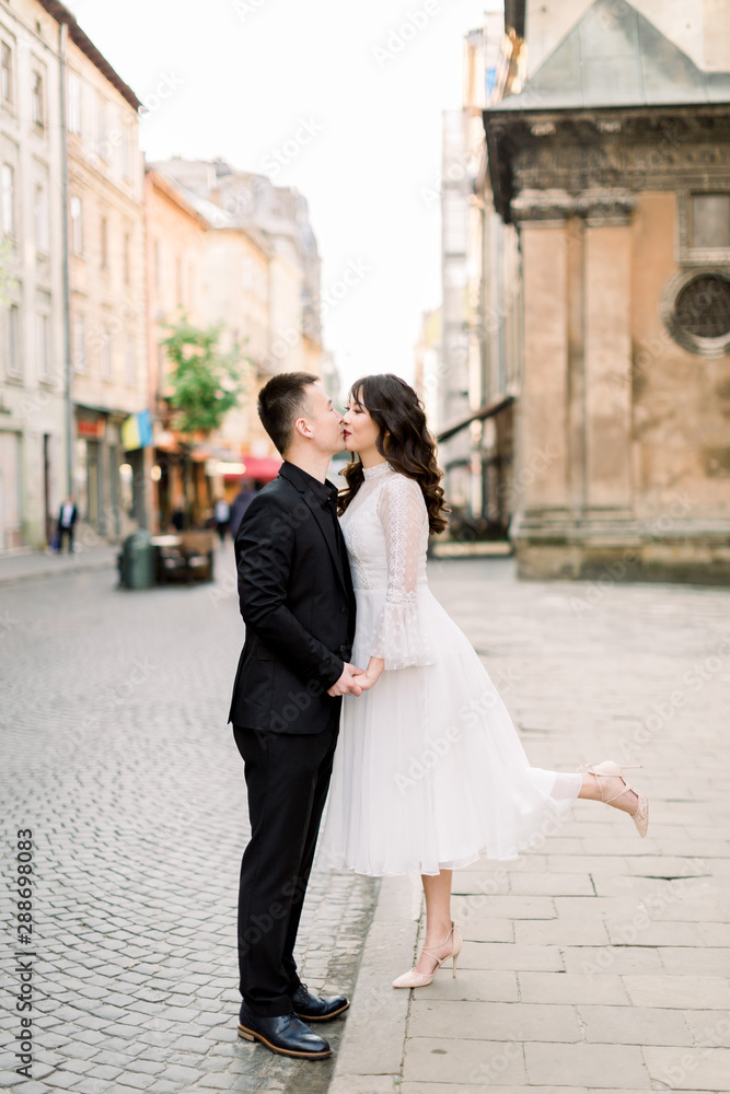 Lovely Asian couple walk and kissing in the city. Man is in black luxury suit, woman in white stylish dress