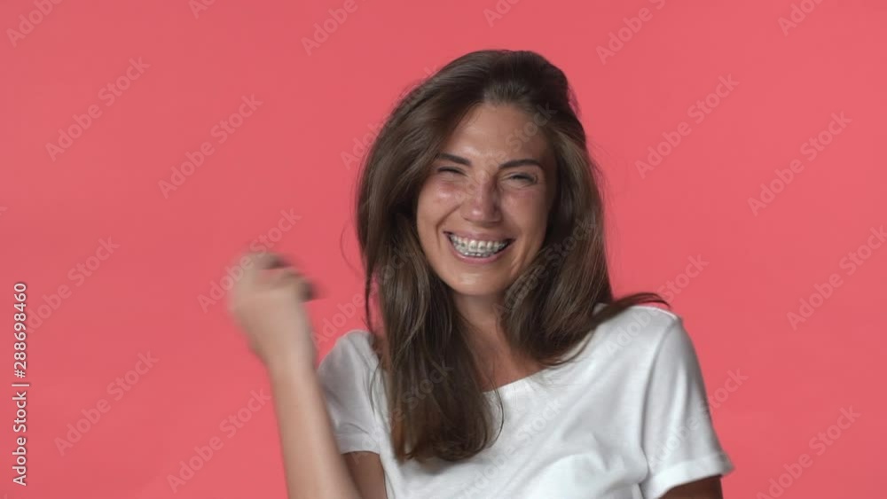 Silly carefree cute adult brunette woman with braces, wear white t-shirt, laughing flirty and silly, smiling joyfully and shaking index finger in refusal or no sign, standing red background