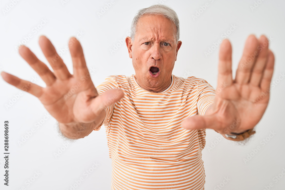 Senior grey-haired man wearing striped t-shirt standing over isolated white background doing stop gesture with hands palms, angry and frustration expression Senior grey-haired man wearing striped t-shirt standing over isolated white background doing stop gesture with hands palms, angry and frustration expression