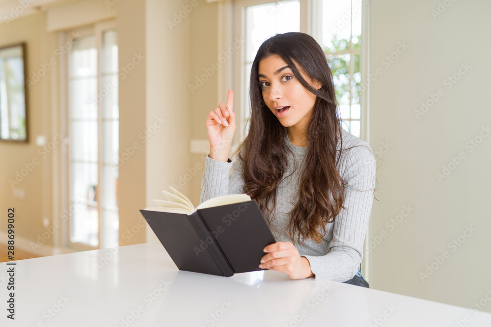 Young woman reading a book surprised with an idea or question pointing finger with happy face, number one Young woman reading a book surprised with an idea or question pointing finger with happy face, number one