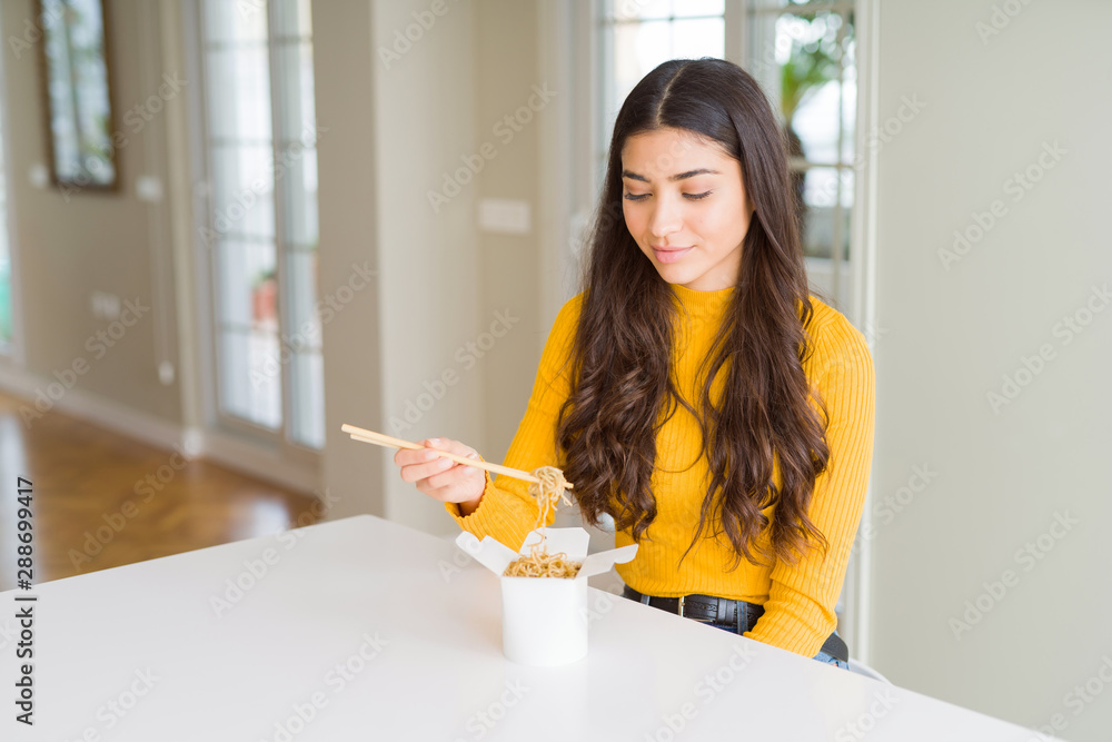 Young woman eating noodles in delivery box with a confident expression on smart face thinking serious Young woman eating noodles in delivery box with a confident expression on smart face thinking serious