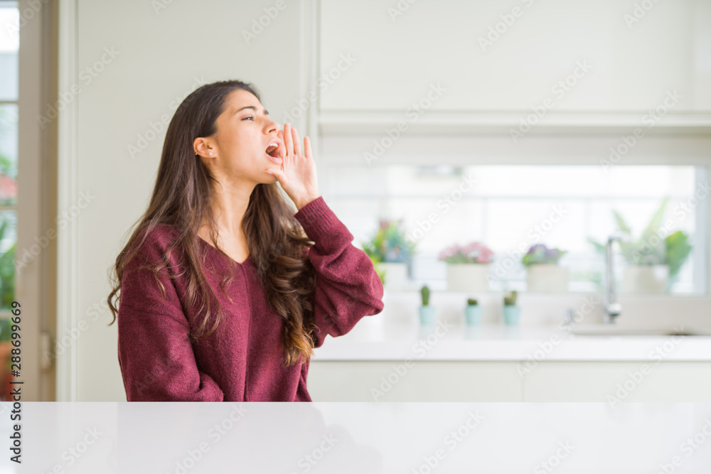 Young beautiful woman at home shouting and screaming loud to side with hand on mouth. Communication concept. Young beautiful woman at home shouting and screaming loud to side with hand on mouth. Communication concept.