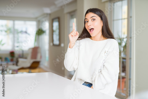 Free Download Young beautiful woman at home on white table pointing finger up with successful idea. Exited and happy. Number one. - GFXLoad