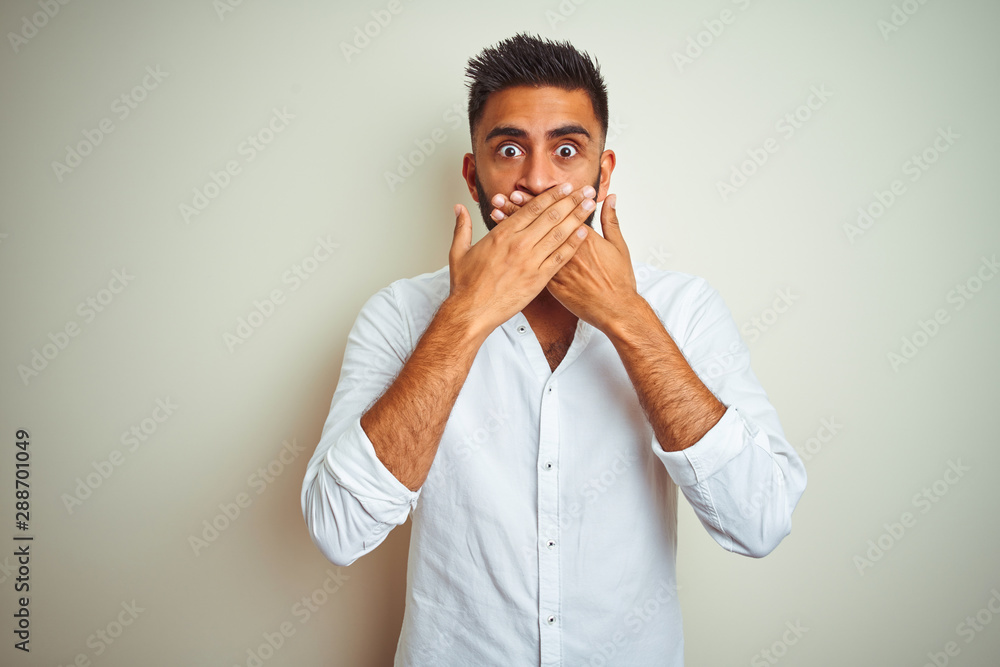 Young indian man wearing elegant shirt standing over isolated white background shocked covering mouth with hands for mistake. Secret concept. Young indian man wearing elegant shirt standing over isolated white background shocked covering mouth with hands for mistake. Secret concept.