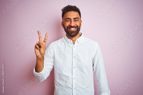Young indian businessman wearing elegant shirt standing over isolated pink background showing and pointing up with fingers number two while smiling confident and happy.