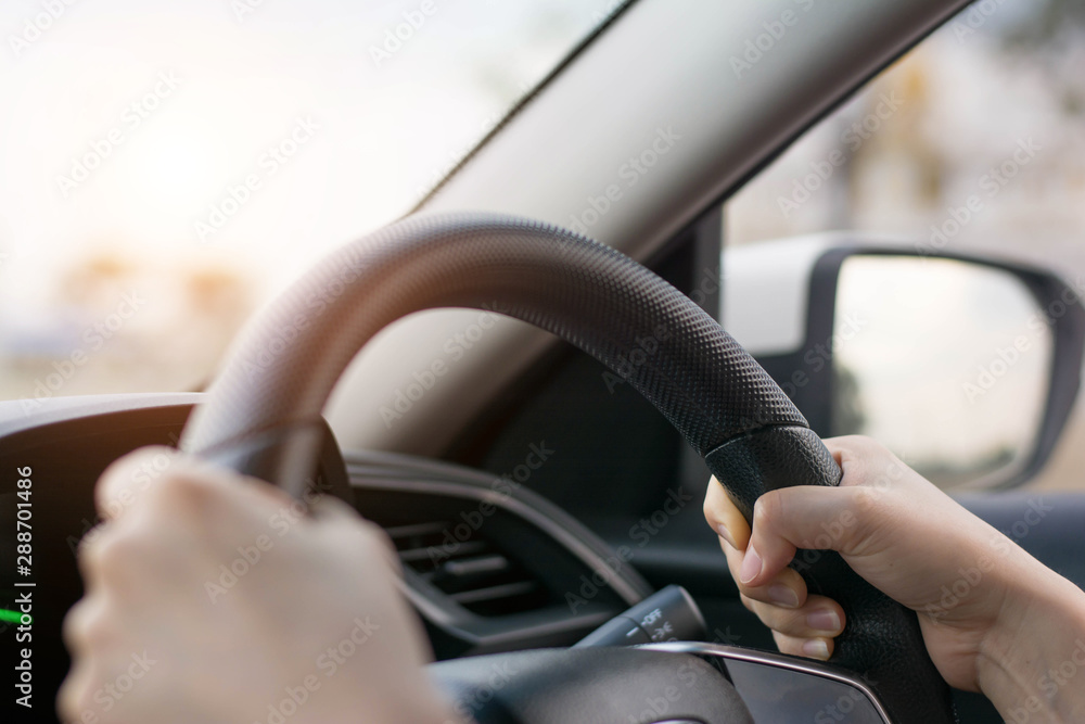 Female hands on the steering wheel of a car while driving. Against the background, the windshield and road,Close-up of a woman's hand driving a car