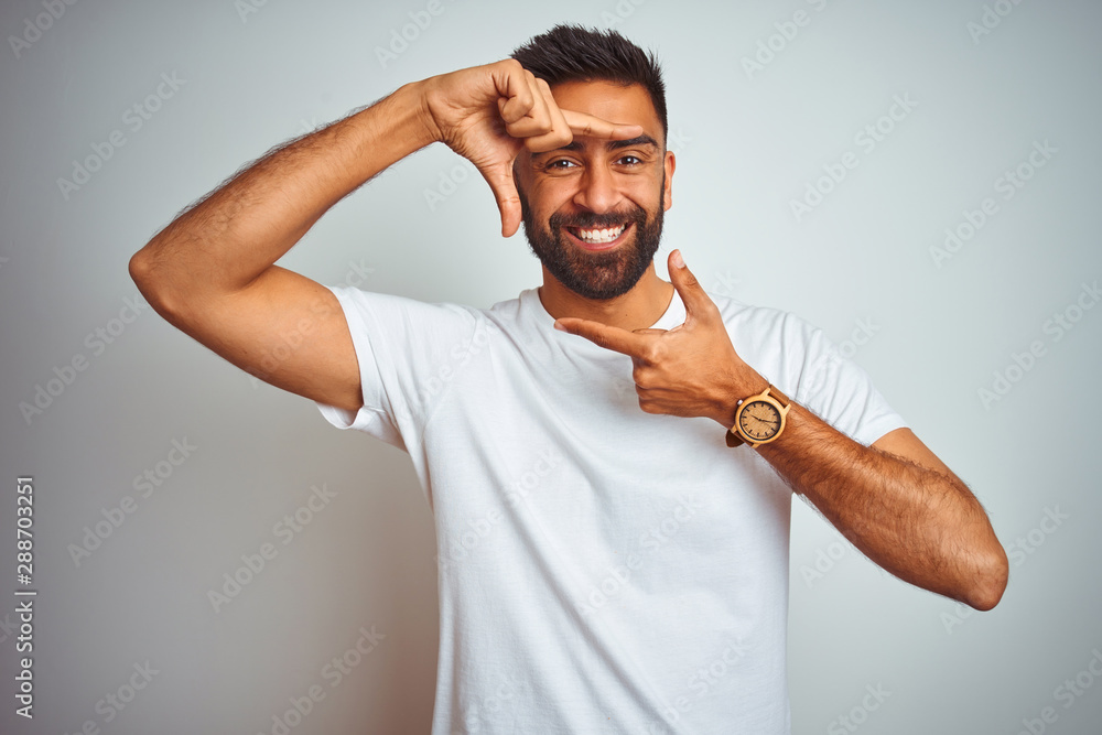 Young indian man wearing t-shirt standing over isolated white background smiling making frame with hands and fingers with happy face. Creativity and photography concept. Young indian man wearing t-shirt standing over isolated white background smiling making frame with hands and fingers with happy face. Creativity and photography concept.