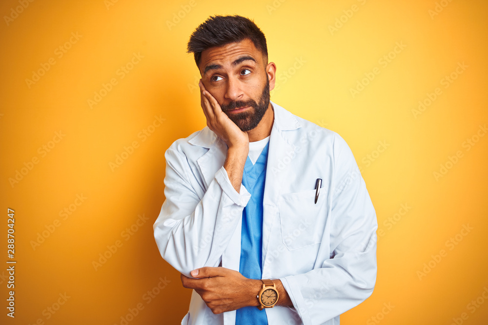 Young indian doctor man standing over isolated yellow background thinking looking tired and bored with depression problems with crossed arms. Young indian doctor man standing over isolated yellow background thinking looking tired and bored with depression problems with crossed arms.