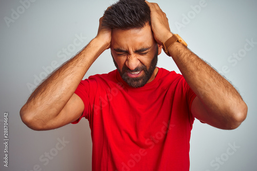 Fotografie Young indian man wearing red t-shirt over isolated white background suffering from headache desperate and stressed because pain and migraine
