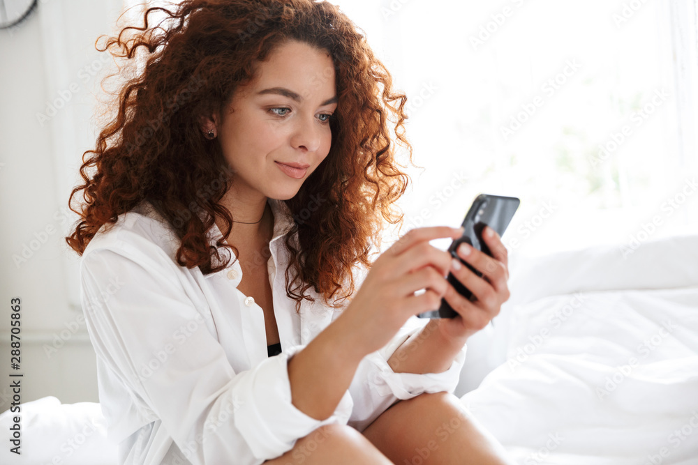 Woman dressed in white shirt indoors in home hotel in bed using mobile phone. Woman dressed in white shirt indoors in home hotel in bed using mobile phone.