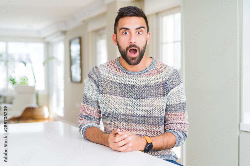 Handsome hispanic man wearing casual sweater at home afraid and shocked with surprise expression, fear and excited face.