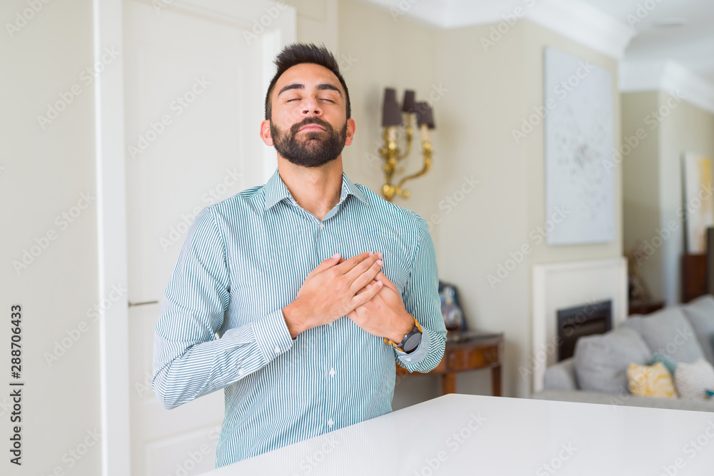 Handsome hispanic man at home smiling with hands on chest with closed eyes and grateful gesture on face. Health concept.