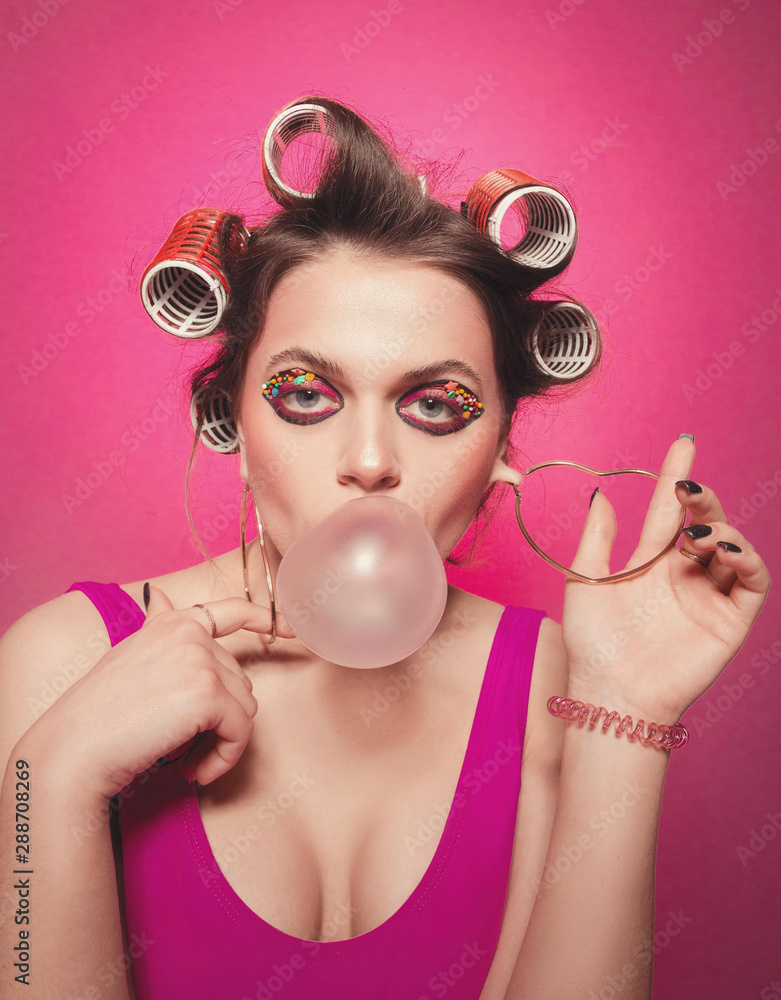 Cheeky girl with bubble gum posing on pink background in body, with curlers  on head. Pretty woman with sweet makeup making balloons with bubblegum in  studio Stock Photo | Adobe Stock