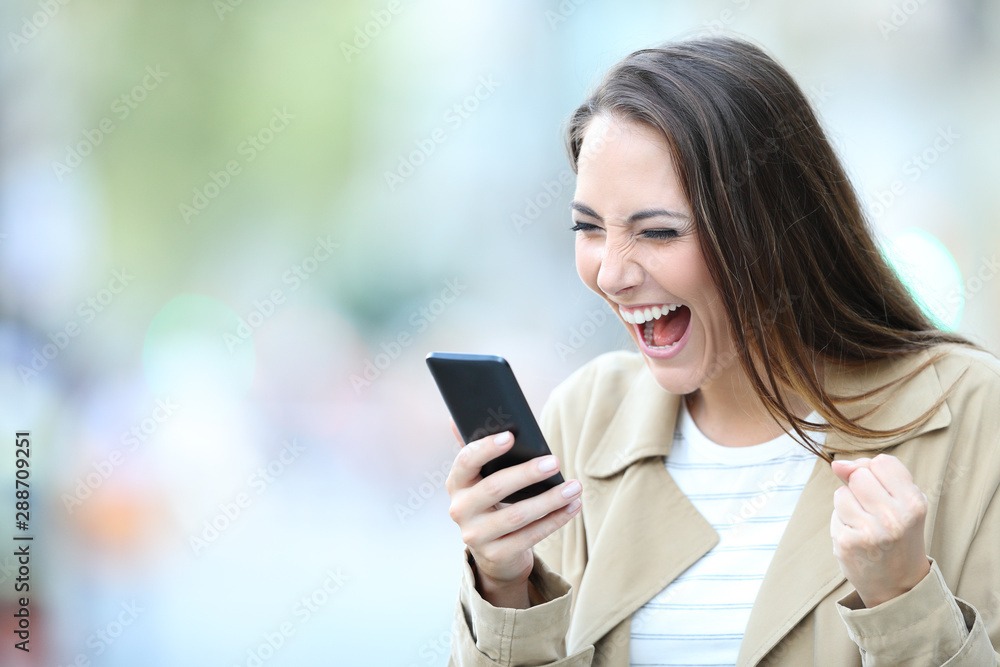 Excited woman finds good offers on phone in the street Excited woman finds good offers on phone in the street