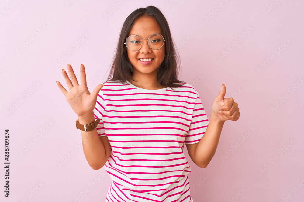 Young chinese woman wearing striped t-shirt and glasses over isolated pink background showing and pointing up with fingers number six while smiling confident and happy. Young chinese woman wearing striped t-shirt and glasses over isolated pink background showing and pointing up with fingers number six while smiling confident and happy.