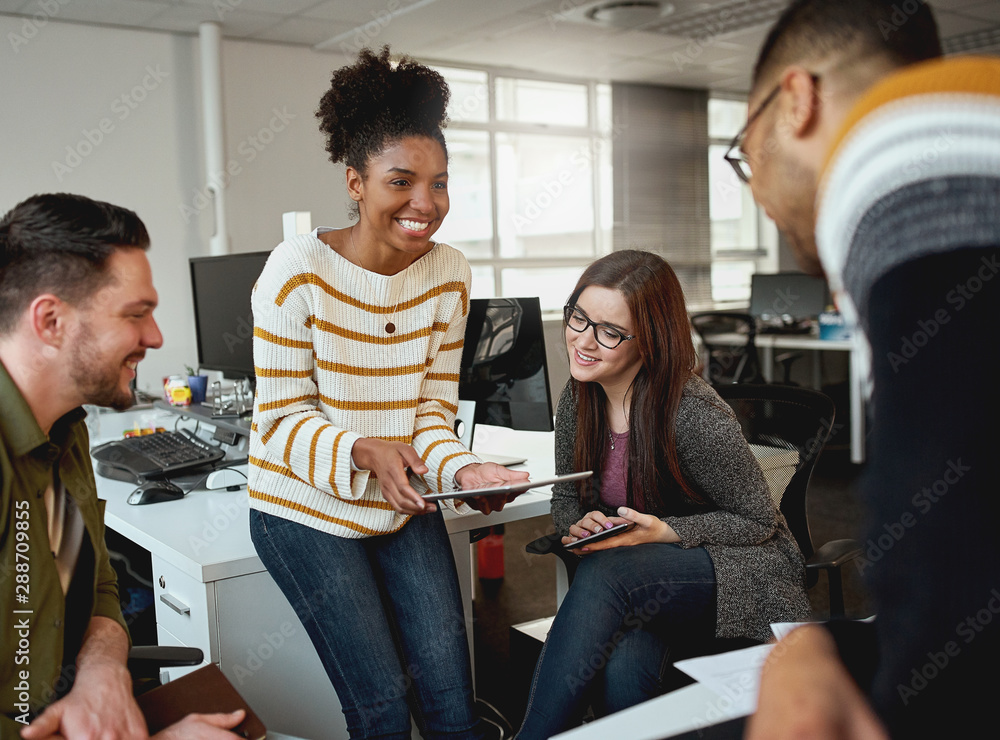 © StratfordProductions - Creative young woman showing business plan on digital tablet to colleagues during a meeting in front of business group - start up company