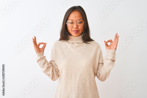 Young chinese woman wearing turtleneck sweater and glasses over isolated white background relax and smiling with eyes closed doing meditation gesture with fingers. Yoga concept.