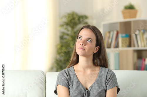 Serious woman dreaming looking at side sitting at home