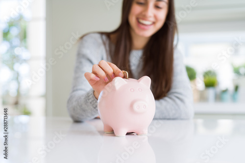 Young woman smiling putting a coin inside piggy bank as savings for investment