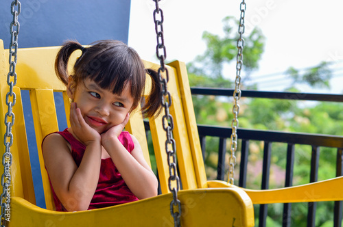 Asian children girl sitting on a yellow swing.