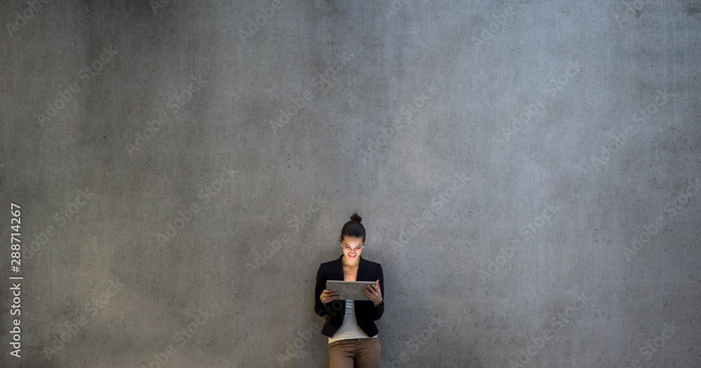 Young business woman with tablet standing against concrete wall in office. - obrazy, fototapety, plakaty 