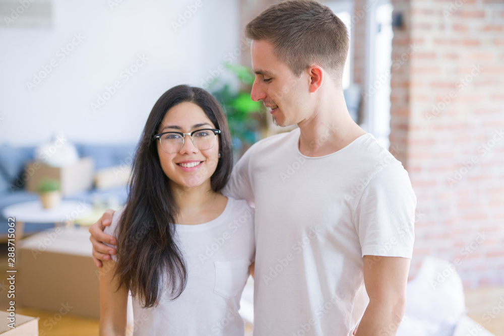 Young beautiful couple standing at new home around cardboard boxes Young beautiful couple standing at new home around cardboard boxes