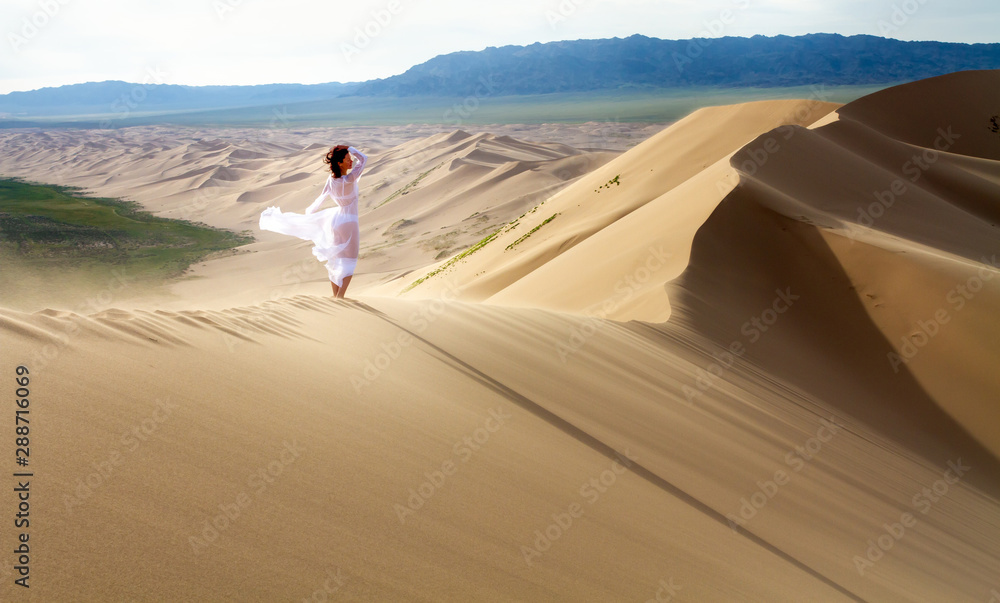 Fototapeta premium Woman walking in the mongolian desert sand dunes. Young woman walking golden sand on a bright summer day, Mongolia holliday vacation concept.
