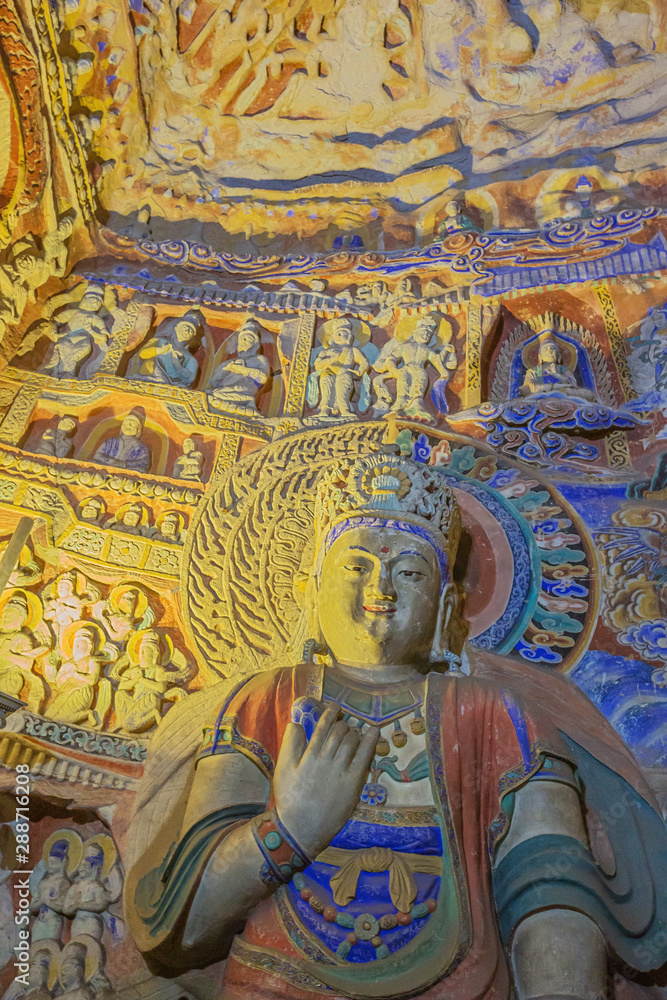 Weathered colorful Buddha with little statues in cave 9 of the Yungang Grottoes near Datong