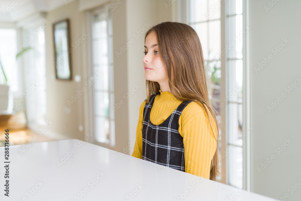Beautiful young girl kid sitting on the table looking to side, relax profile pose with natural face with confident smile.