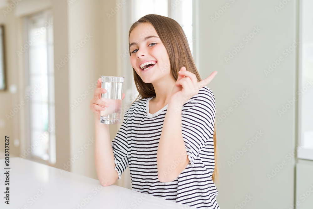 Beautiful young girl kid drinking a fresh glass of water very happy pointing with hand and finger to the side Beautiful young girl kid drinking a fresh glass of water very happy pointing with hand and finger to the side