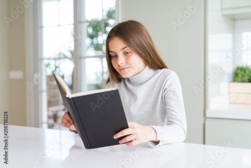 Beautiful young girl reading a book at home with a confident expression on smart face thinking serious