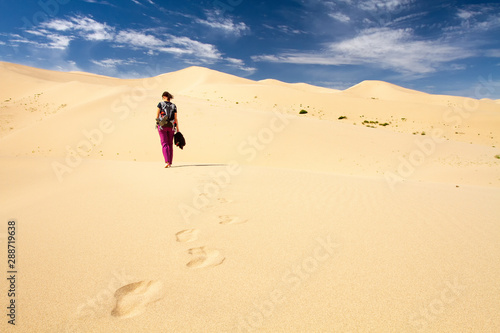 Woman walking in the mongolian desert sand dunes. Young woman walking golden sand on a bright summer day  Mongolia holliday vacation concept.