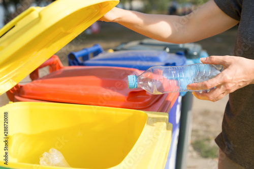 The girl is disposing of recycled garbage from glass plastic bottles in a trash can. 